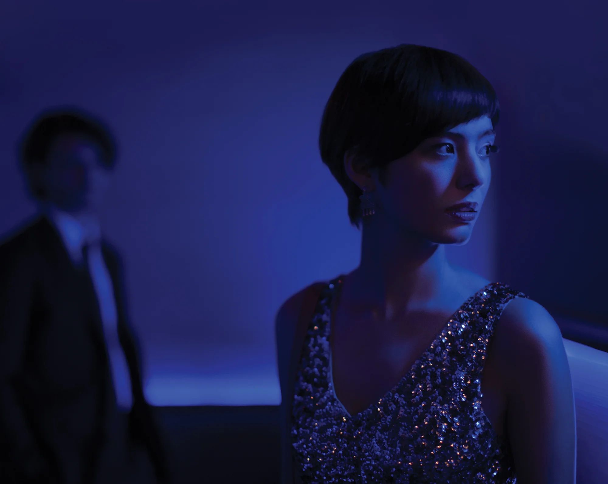 Still from MAKI: a woman in a beaded dress against a deep blue interior.